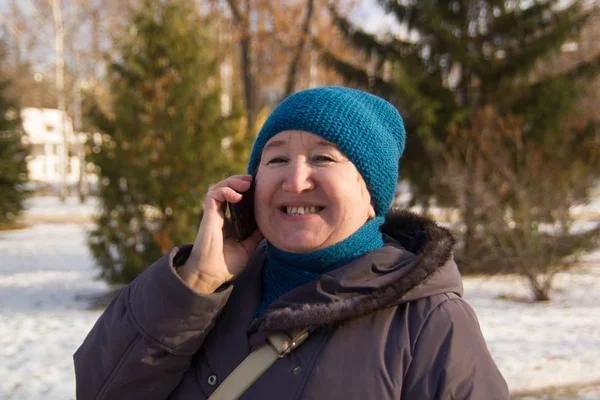 Портрет взрослой женщины, разговаривающей по телефону на открытом воздухе. Старшая леди улыбается и в парке в зимний солнечный день — стоковое фото