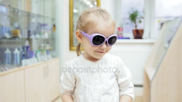 Маленькая девочка пробует медицинские синие очки - покупки в клинике — стоковое видео