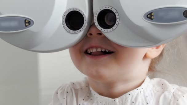 Adorable little blonde girl checks eyesight at ophthalmology clinic — Stock Video