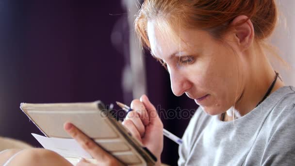 Retrato de mujer en casa sentada en el sofá y trabajando con gadget y notebook — Vídeos de Stock