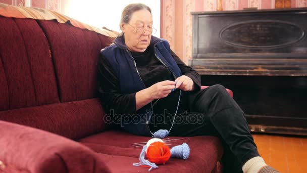 Femme âgée assise sur le canapé et tricote de la laine colorée - passe-temps des retraités à la maison, slider shot — Video