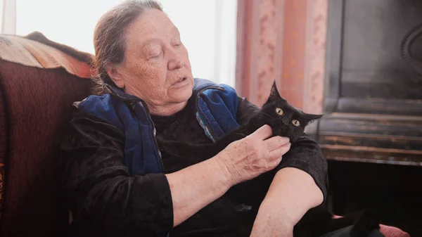 Retrato de senhora idosa em casa - senhora idosa senta-se no sofá com gato preto - close up — Fotografia de Stock
