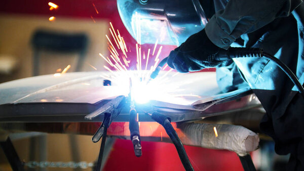 Welding industrial: worker in helmet repair detail in car service