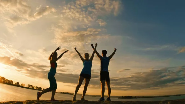 Gruppen för ung man och kvinnor - idrottare - två tjejer och en kille är har triumph på berget, nära floden i skymningen — Stockfoto
