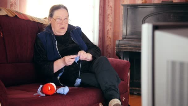 Портрет пожилой женщины, смотрящей телевизор, вяжущей шерстяные носки — стоковое видео