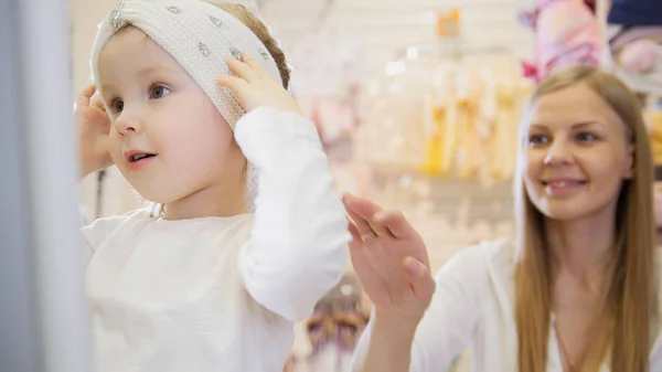 Tienda de vestir Babys - pequeña niña rubia con madre haciendo compras y comprando sombrero bonito — Foto de Stock