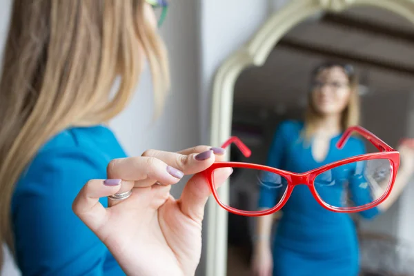 Vacker ung kvinna med röda glasögon nära spegel - oftalmologi-konceptet — Stockfoto