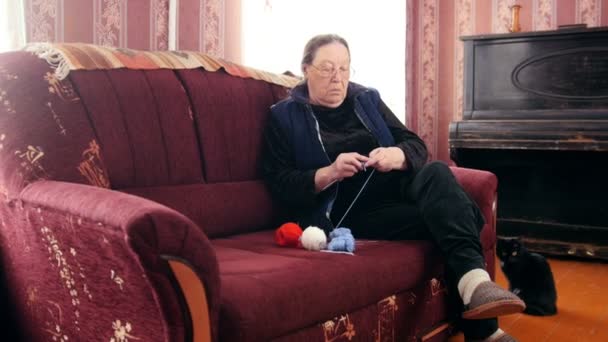 Femme âgée assise sur le canapé et tricote de la laine colorée - passe-temps des retraités à la maison, slider shot — Video