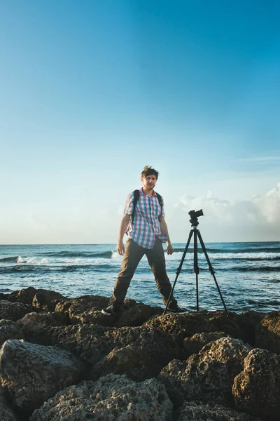 A young man stands on the coast, and photographing nature with the camera on a tripod Royalty Free Stock Images