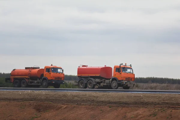 Trabajos de construcción de carreteras: dos camiones de riego rojo en la carretera entre el campo — Foto de Stock