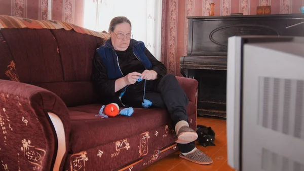 Maison de vieille dame au canapé regarder la télévision et tricoter des chaussettes en laine — Photo