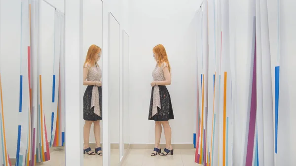Meisje in kledingwinkel kiest jurk in de buurt van spiegel in kamer - shopping concept passen — Stockfoto