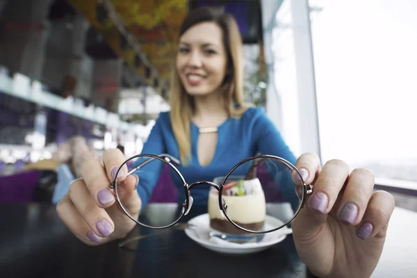 Ganska ung flicka håller glasögon i händer sitter i café, oftalmologi — Stockfoto