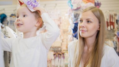 Alışveriş ve çocuk elbise mağazası şapka satın alma yaparken anne ile küçük sarışın bebek kız