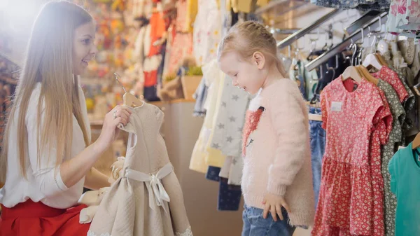 Hija con madre comprando ropa para niños en la tienda — Foto de Stock