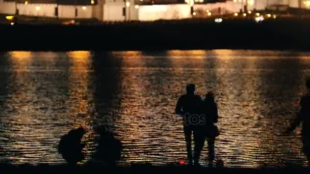 Personas en la ciudad nocturna cerca del río - luces nocturnas de fondo — Vídeo de stock