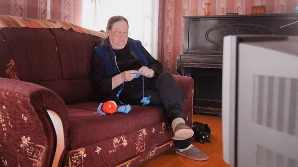 Пожилая женщина в очках вязала перед телевизором — стоковое фото