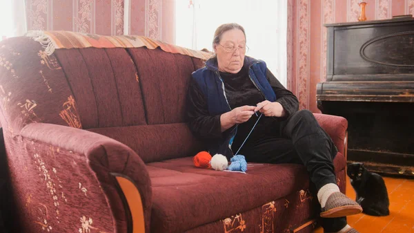 Пожилая женщина в очках дома вяжет шерсть — стоковое фото