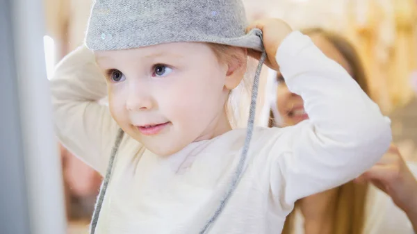 Het kleine meisje voor een spiegel het dragen van een grijze muts. — Stockfoto
