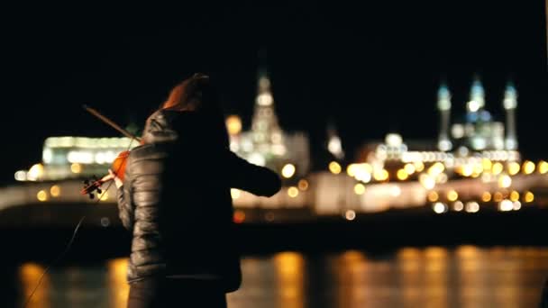 Силует жінки скрипаль грає на скрипці в нічному місті в холодну пору року — стокове відео