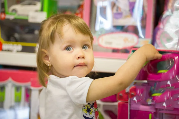 Feliz niña elige juguetes en una tienda de niños — Foto de Stock