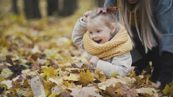 Madre y su hija pequeña jugando en un parque de otoño - tirar las hojas, risas bebé — Foto de Stock