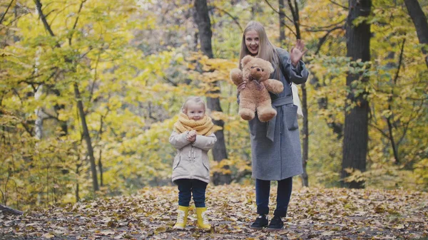 Hijita con su madre y su osito de peluche caminando en el parque de otoño — Foto de Stock