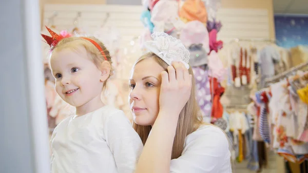 Niños de compras - mamá se prueba una diadema blanca junto a su hija — Foto de Stock