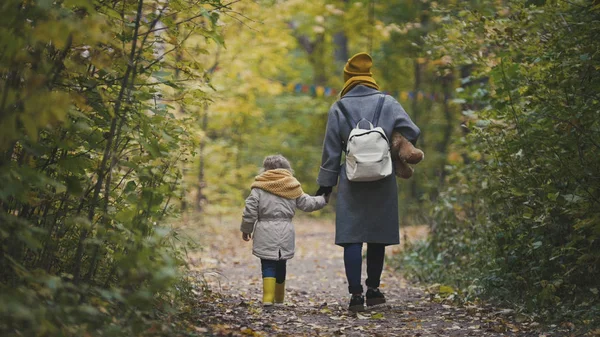 Joven madre y su hija niña se alejan en un parque de otoño — Foto de Stock