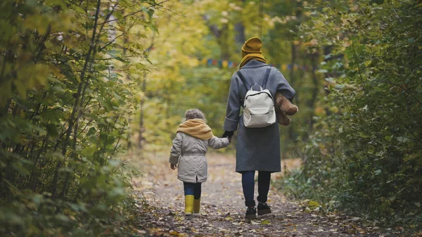 Ung mamma och hennes dotter lilla flicka flyttar bort i en höst park — Stockfoto