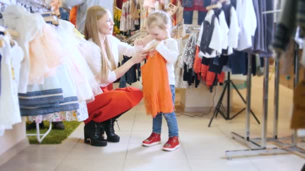 Ένα μικρό κορίτσι που προσπαθεί σε ένα κόκκινο φόρεμα - παιδική ψώνια — Αρχείο Βίντεο