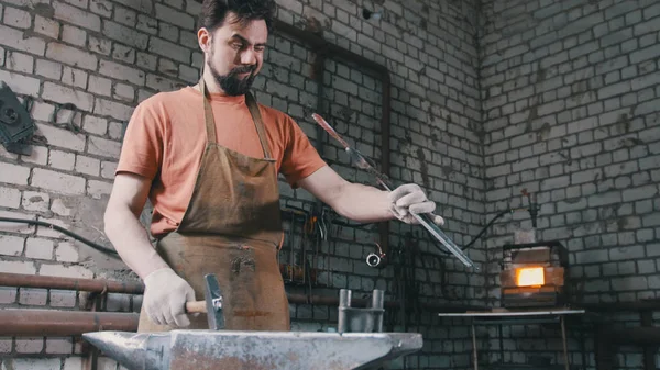 Herrero hombre musculoso con martillo en forja creando cuchillo de acero —  Fotos de Stock