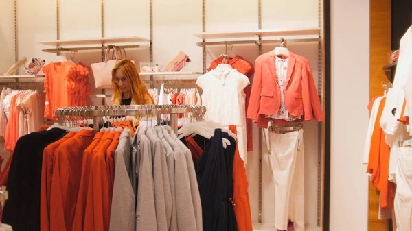 Una mujer elige un traje en una tienda de ropa para mujeres —  Fotos de Stock