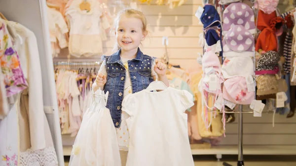 Comprando para niños. La chica está de pie cerca del espejo y sosteniendo perchas con ropa — Foto de Stock