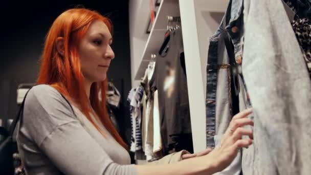 Een vrouw kiest kleding in winkelcentrum — Stockvideo