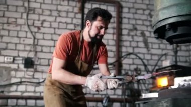 Bir Demirci Atölyesi. Bir adam bir otomatik çekiç altında sahte bir parça koyar