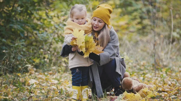 Drobná světlovlasá dívka s její maminkou v podzimním parku - hrát a tleskat rukama, zblízka — Stock fotografie