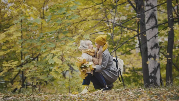 Madre e hija juntas entre hojas amarillas en el parque de otoño — Foto de Stock
