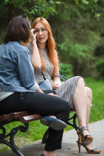 Две девушки сидят на скамейке в парке — стоковое фото