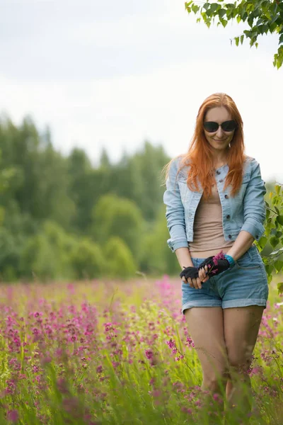 Рыжая девушка стоит на цветочной поляне — стоковое фото