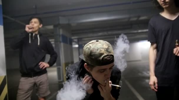 Een jongen in de kring van vrienden op de parkeerplaats waait rook uit zijn mond — Stockvideo