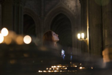 Bir kadın bir Katolik kilisesinde duruyor. Yakınlarda mum yanıyor