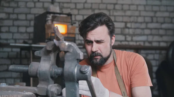 Herrero dobla cuchillo de metal con gripe en taller forja, retrato — Foto de Stock