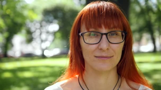 Redhead dziewczyna w okularach flirtuje na trawie w parku — Wideo stockowe