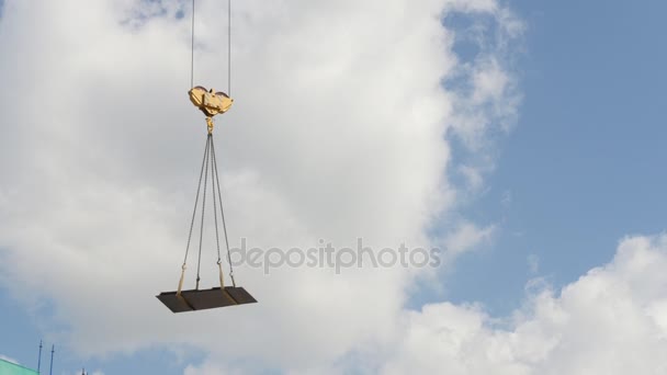 Ein Kran hebt schweres Gerät auf einer Baustelle - vor blauem Himmel — Stockvideo