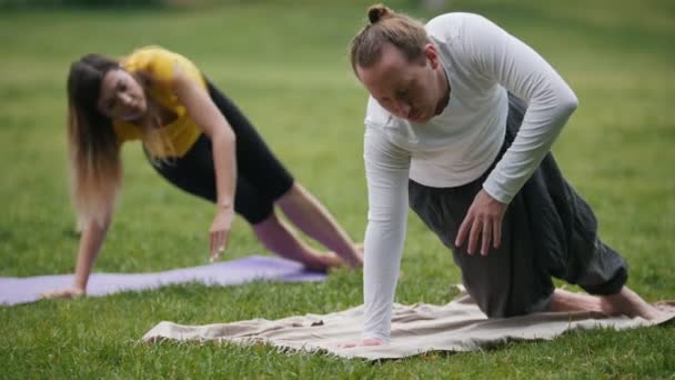 Entrenador de yoga muestra flexibilidad de entrenamiento para señorita en el parque — Vídeos de Stock