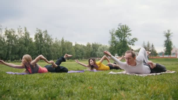 Utomhus yoga träning i parken - mannen och två vackra fitness modeller utför övningarna — Stockvideo