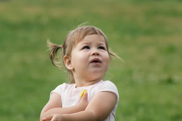 Linda niña pequeña jugando en el parque frente a la hierba verde — Foto de Stock