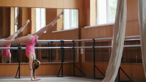 美丽的女孩在套粉红色的西装显示了惊人的灵活性的芭蕾把杆一条腿 — 图库视频影像