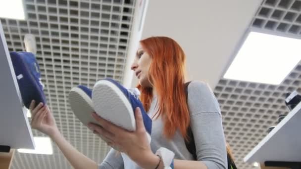 Attractive rd haired woman chooses a sneakers in shoes store - shopping concept — Stock Video